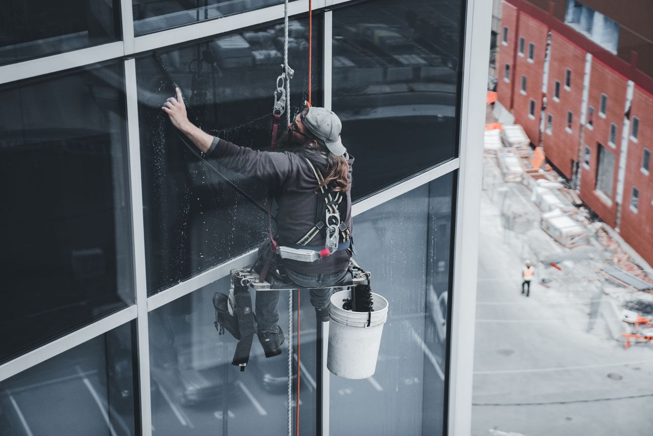 why-choose-us A worker cleaning skyscraper windows with a harness in an urban setting.