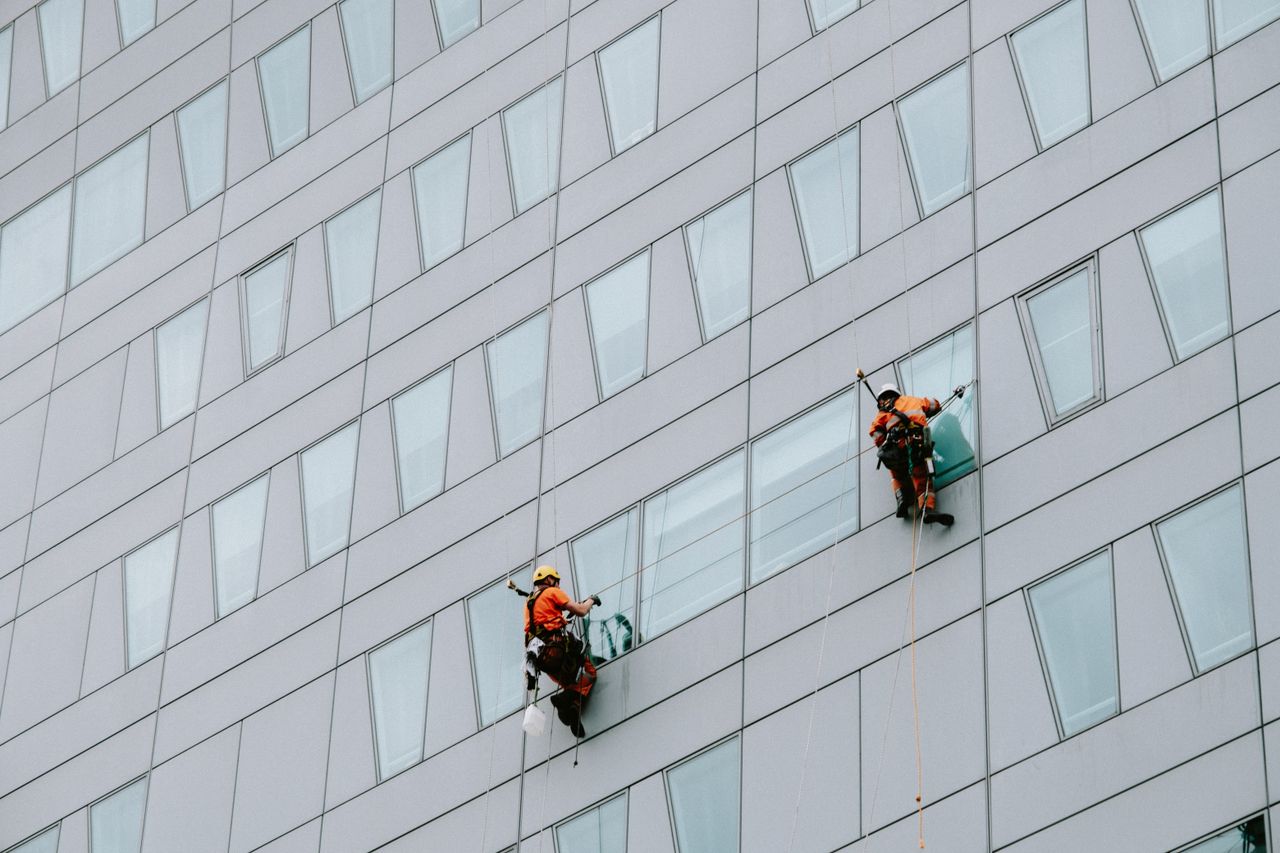 services-03 High-rise window washers in safety gear cleaning a skyscraper facade.